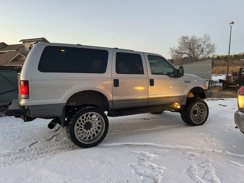 Lifted silver Ford Excursion on large polished wheels in the snow