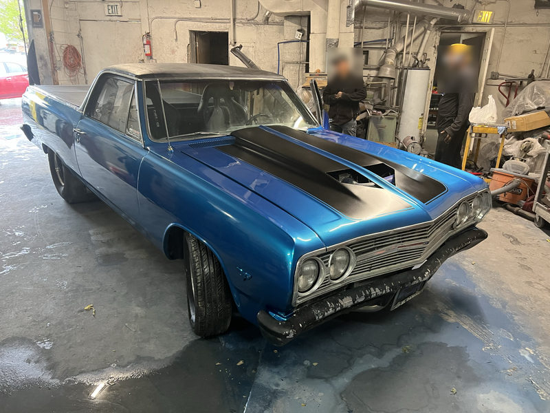 Blue Chevrolet El Camino with a black hood stripe inside a shop