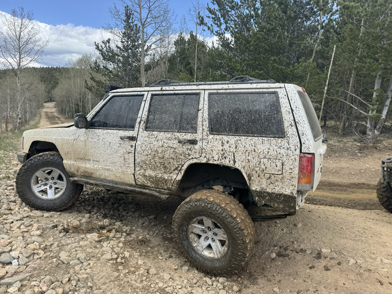 Lifted white Jeep Cherokee covered in mud on a mountain trail